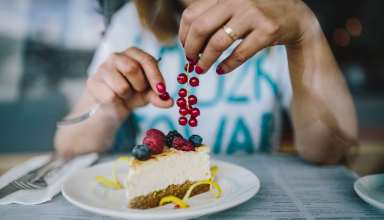 Woman Enjoying Cheese Cake and a Coffee with Fruits in a Cafeteria