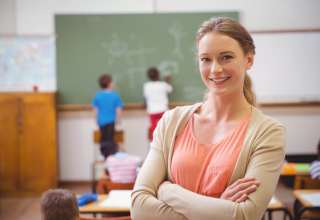 Pretty teacher smiling at camera at back of classroom at the elementary school