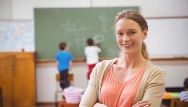 Pretty teacher smiling at camera at back of classroom at the elementary school