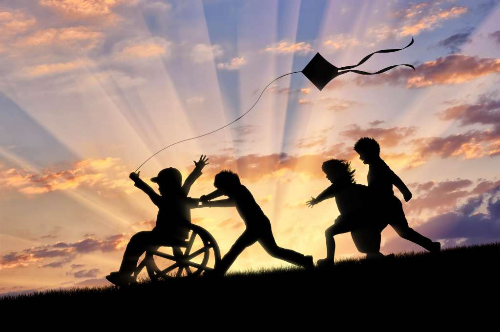 Happy boy in wheelchair playing with children and kite sunset