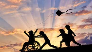 Happy boy in wheelchair playing with children and kite sunset