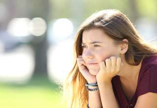 Portrait of angry teen looking sitting alone outside in a park