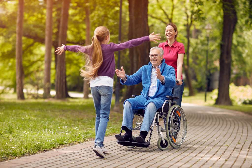 Cheerful grandfather in wheelchair welcoming his happy granddaughter