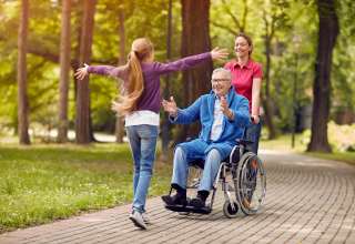 Cheerful grandfather in wheelchair welcoming his happy granddaughter