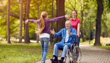 Cheerful grandfather in wheelchair welcoming his happy granddaughter