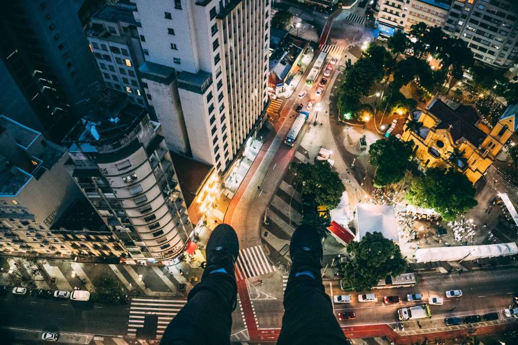 Man Sitting on High Rise Building Taking Photo Below Wallpaper